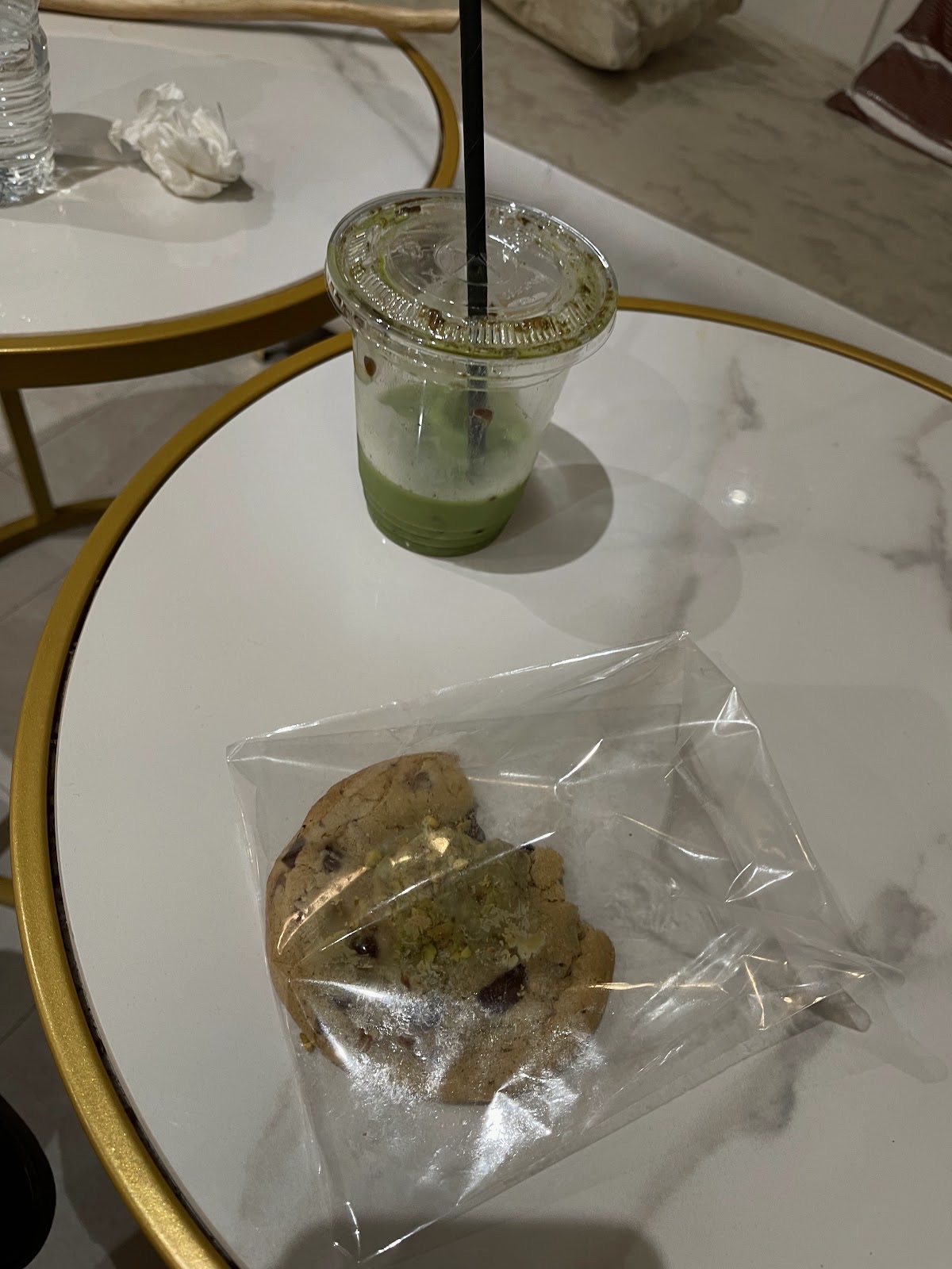 Iced matcha and a wrapped cookie on a gold-rimmed glass side table