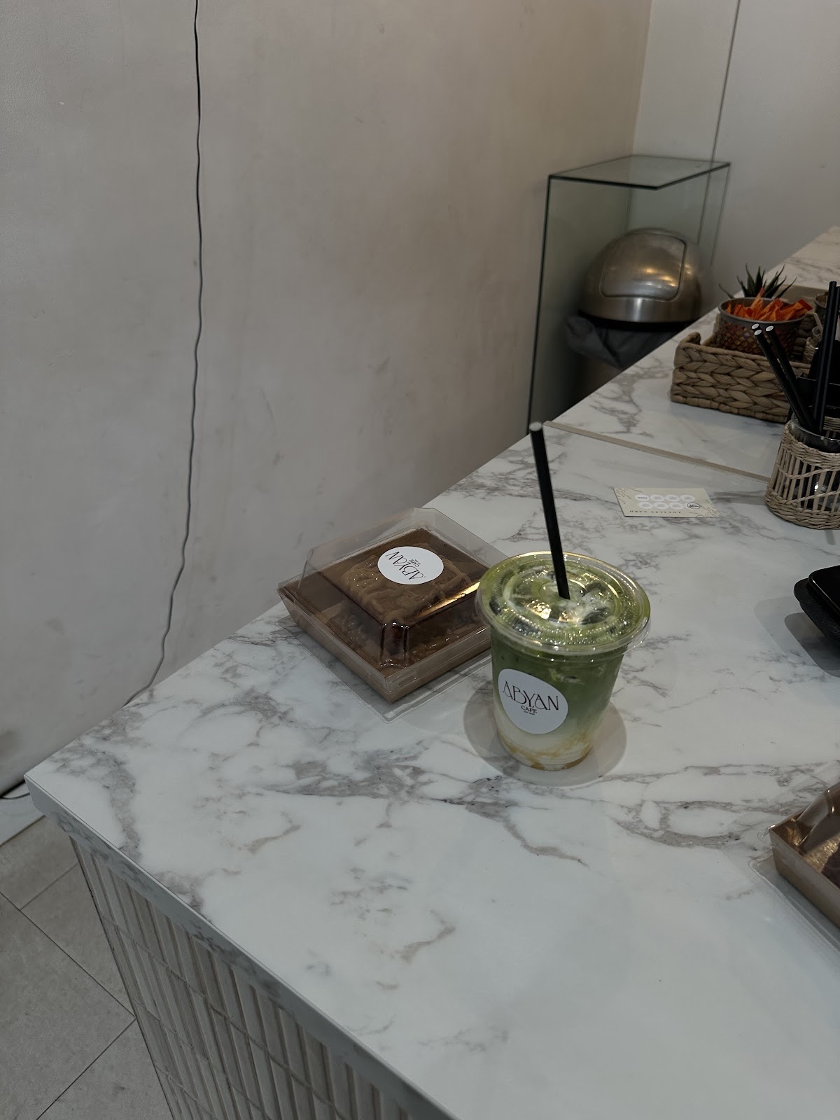 A small matcha drink on the counter beside the display case