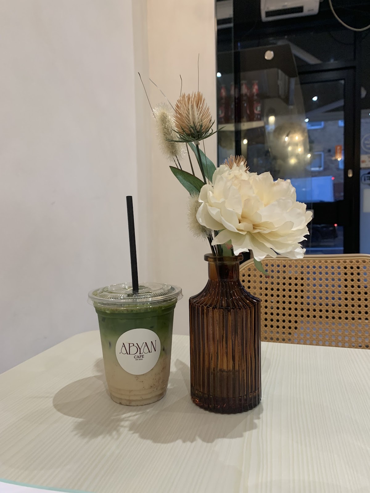 A matcha drink by the window beside a vase of white flowers